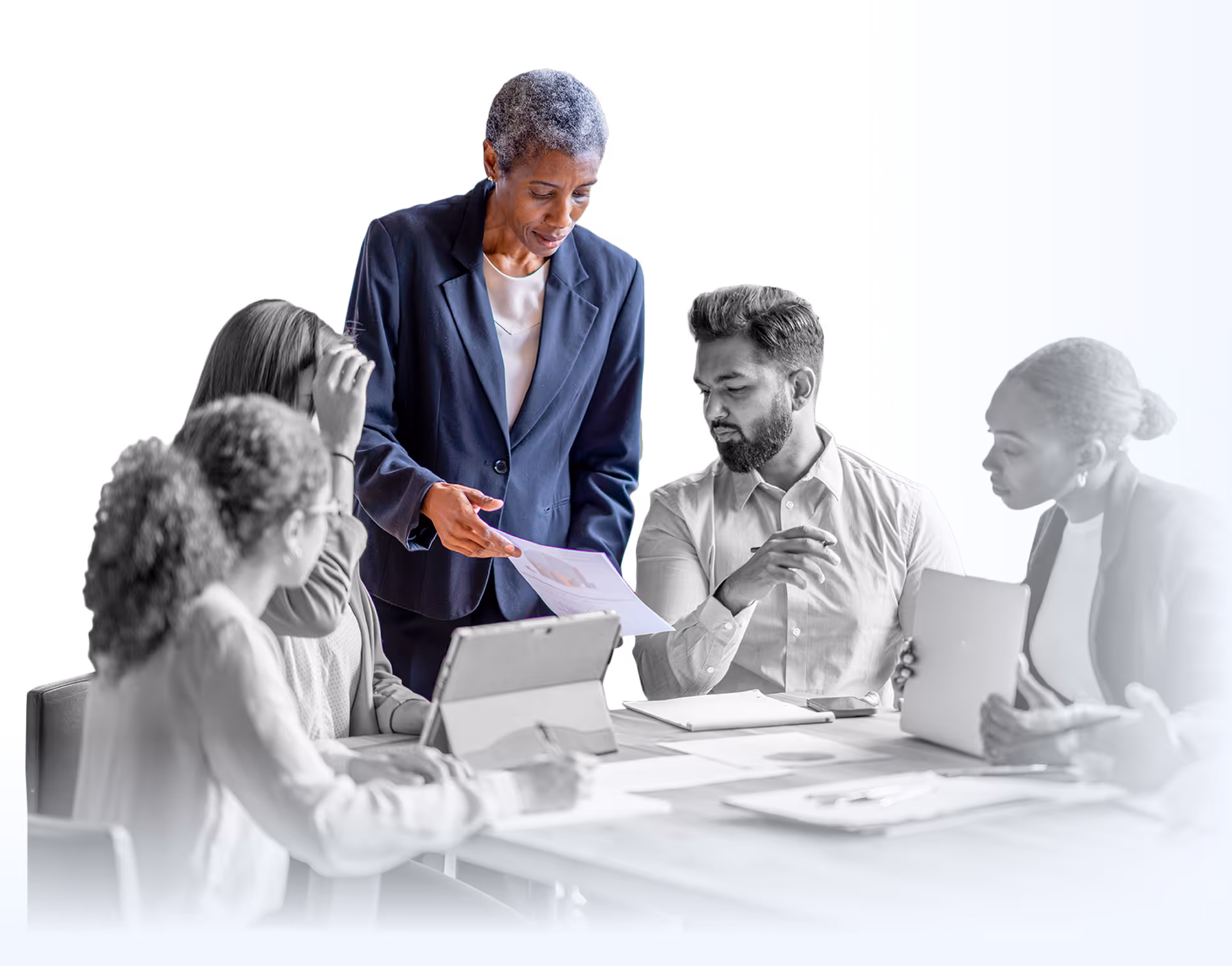 A businesswoman explains a document to colleagues in a meeting with tablets and papers on the table.