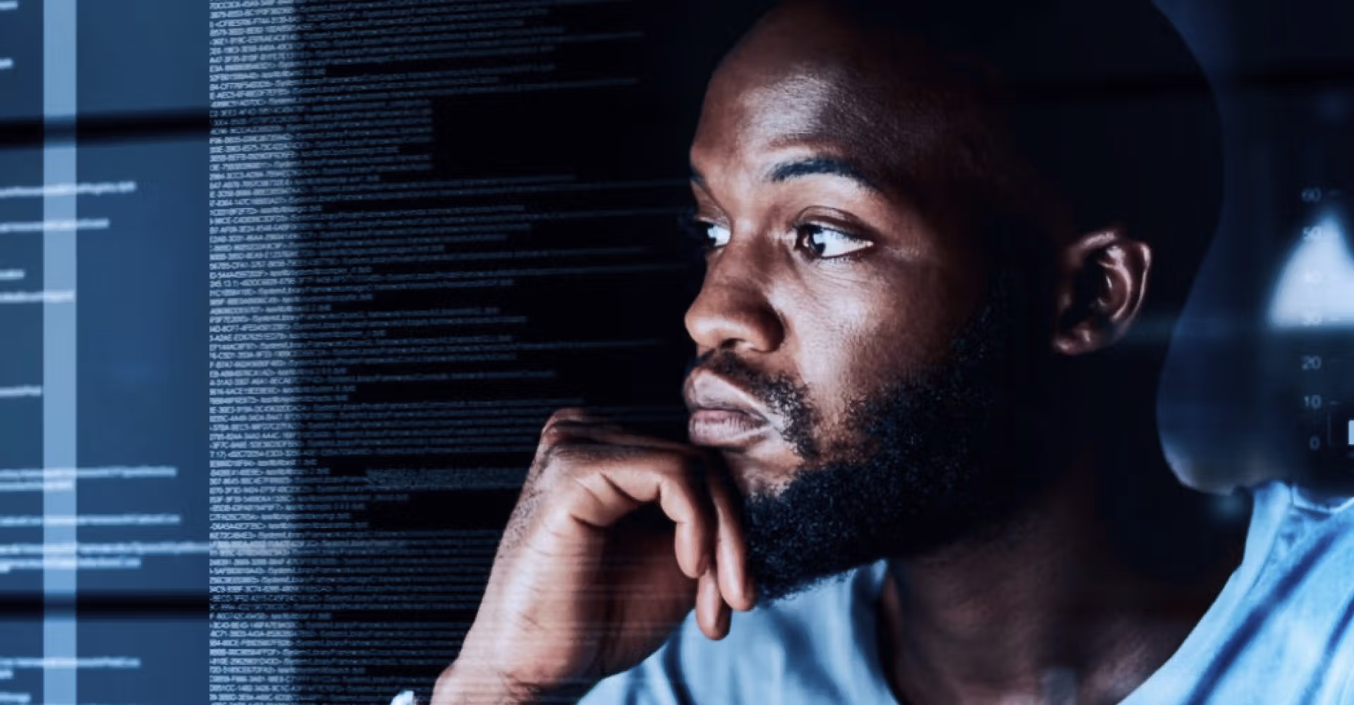 Man with beard looking thoughtfully at computer screen filled with lines of code.