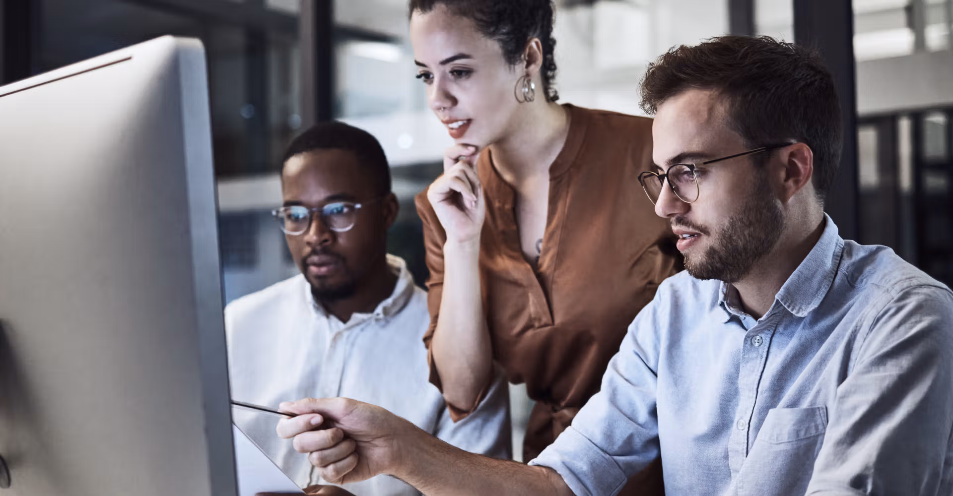 Three colleagues looking intently at a computer screen, one pointing while discussing work.