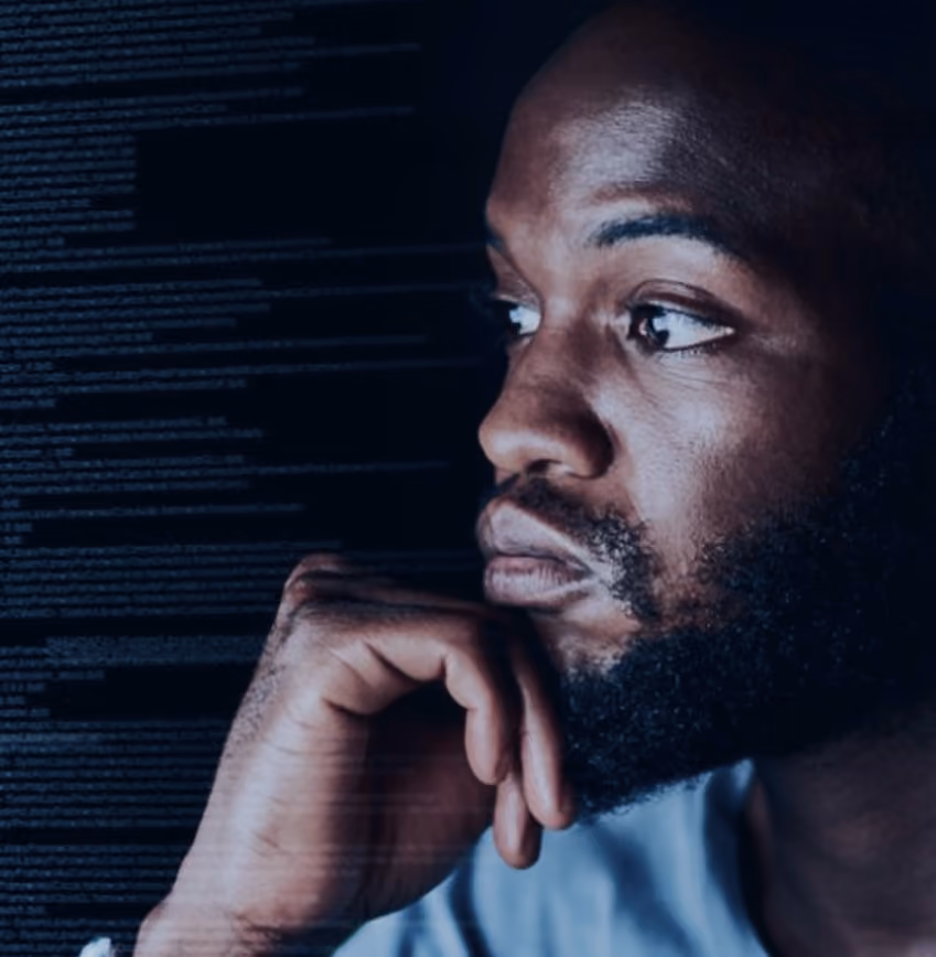 Man with beard looking thoughtfully at computer screen filled with code.