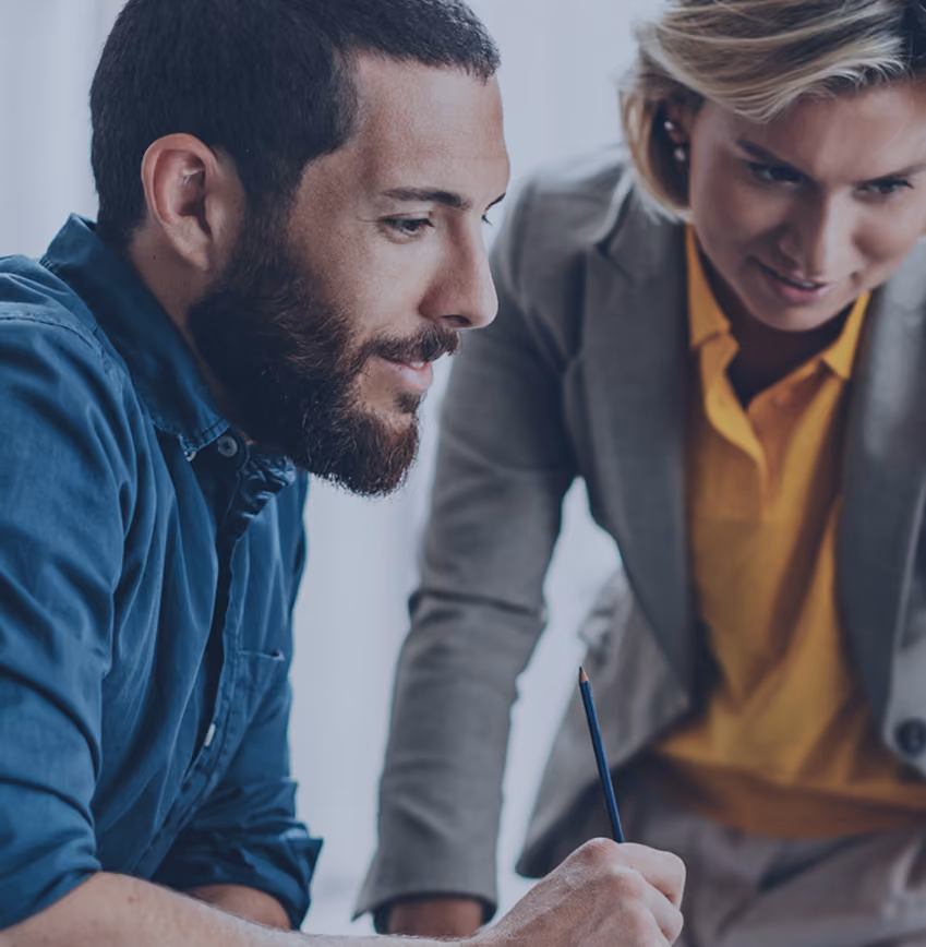 Man with beard and woman in blazer collaborating and looking at a document while working together.