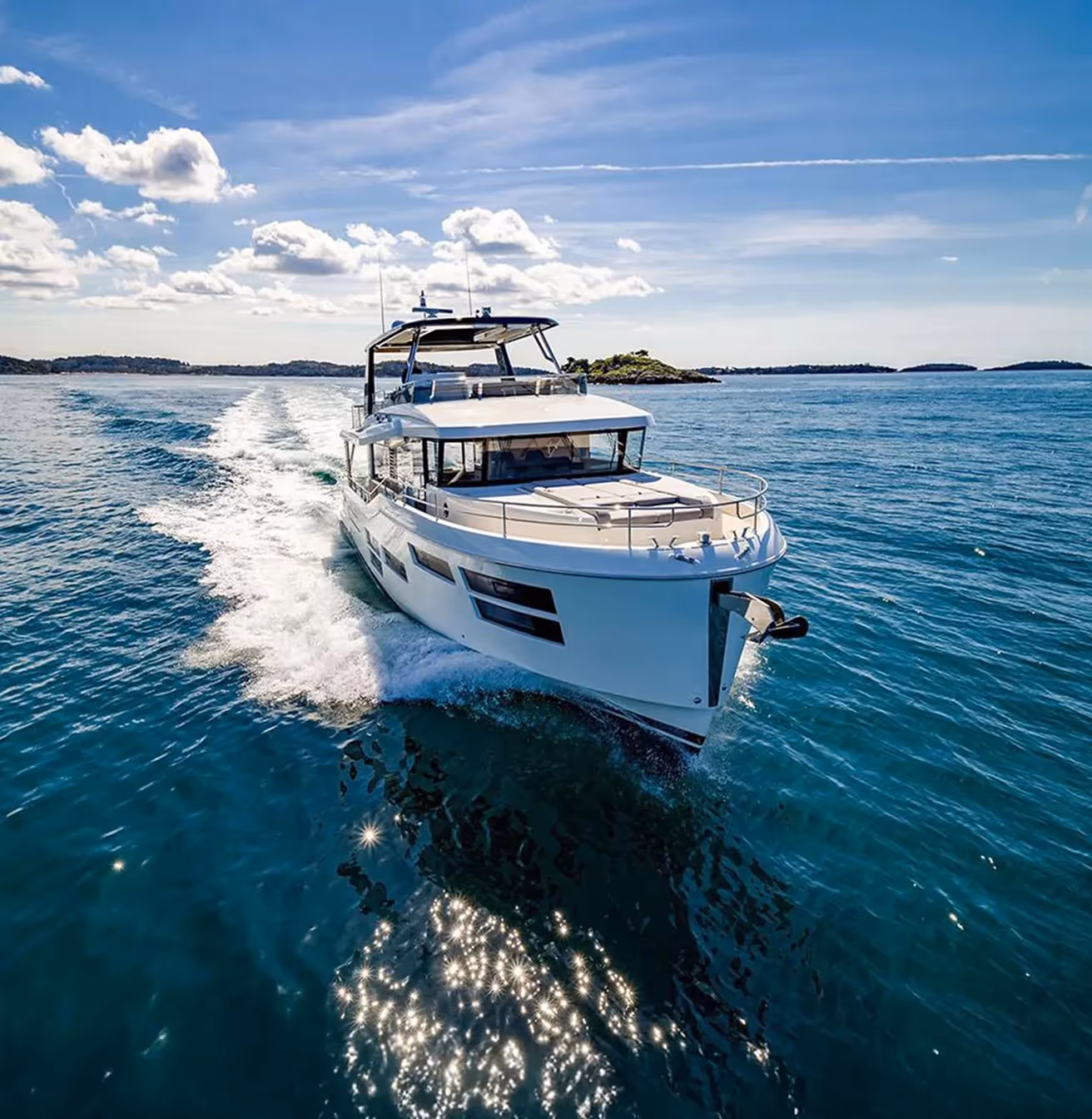 Un yacht blanc naviguant sur une mer calme sous un ciel bleu avec quelques îles à l'horizon.