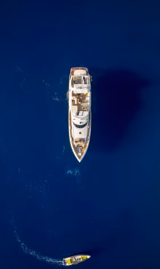 Vue aérienne d'un grand yacht blanc sur une mer bleu foncé avec un petit bateau jaune manœuvrant.