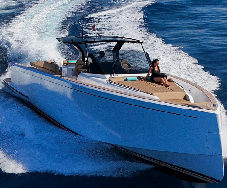 Un yacht blanc rapide avec une femme assise devant, naviguant sur une mer calme et bleue.