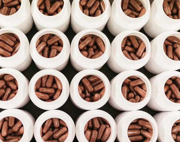 Rows of white bottles filled with brown capsules viewed from above in a grid pattern.