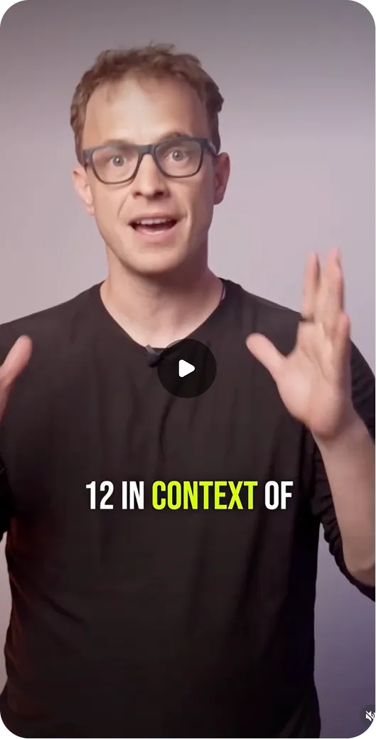 Man with glasses speaking and gesturing with hands in front of a plain background.