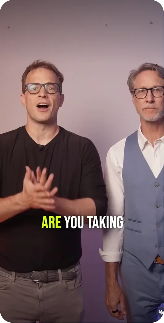 Two men with glasses standing against a plain background, one clapping hands, text 'ARE YOU TAKING'.