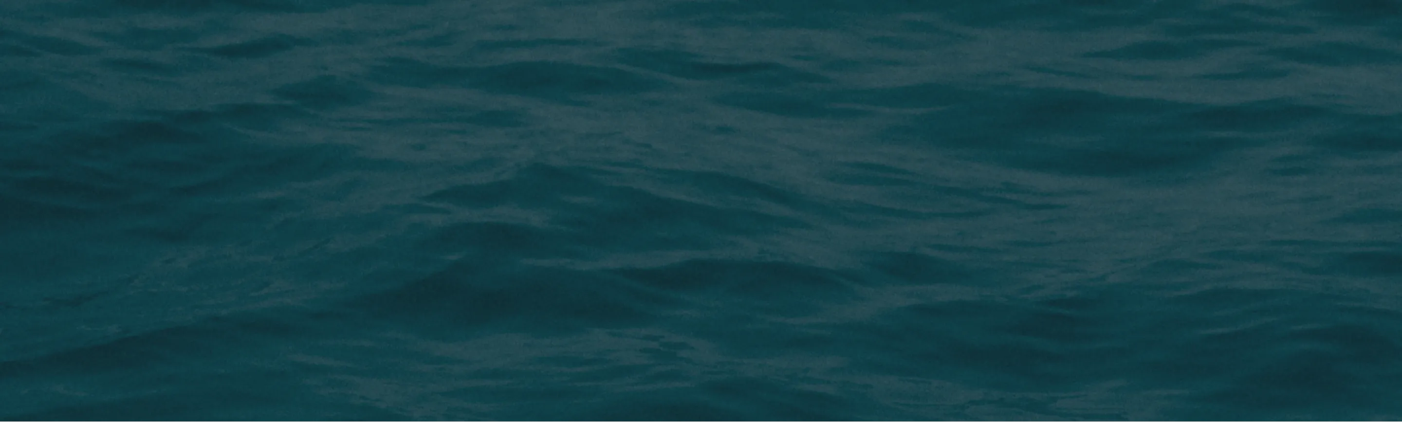 Calm dark blue ocean surface with subtle waves under soft lighting.