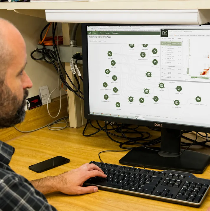 Man using a desktop computer showing a scientific app with green nodes and a heatmap graph on screen.