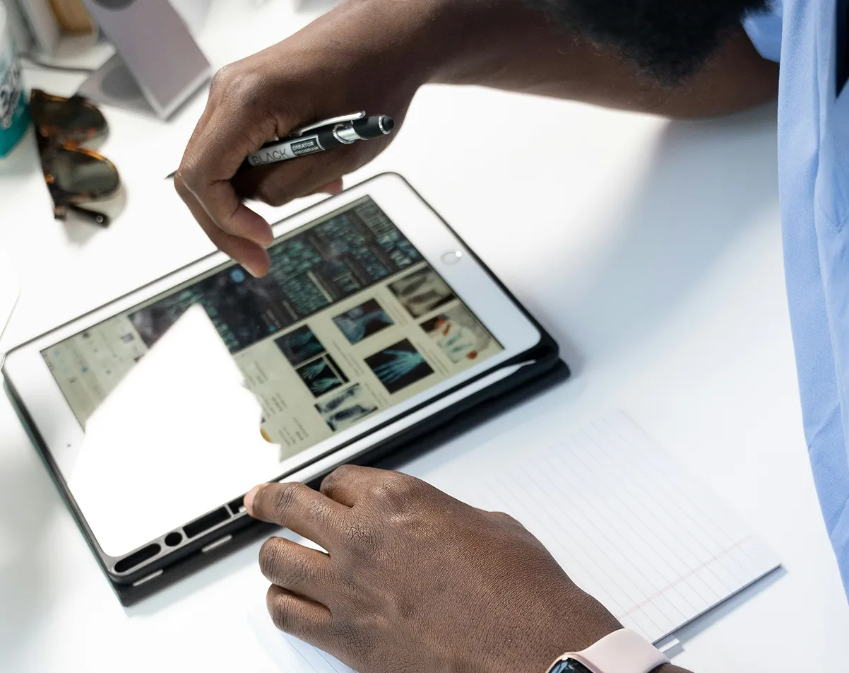 Person holding a pen and examining X-ray images on a tablet on a white table with notebook.