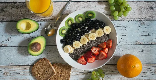 Smoothie bowl with banana, strawberry, kiwi, blackberry, chia seeds, avocado, orange juice, grapes, and bread slices.