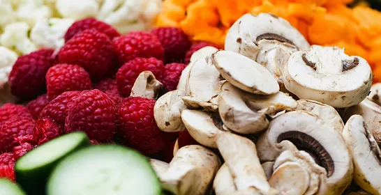Close-up of sliced mushrooms, raspberries, cucumber, and chopped carrots on a colorful vegetable platter.