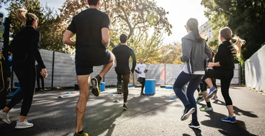 Group of adults exercising outdoors, raising knees during a fitness workout on a sunny day.