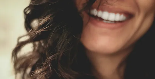 Close-up of a smiling person with curly dark hair showing white teeth.