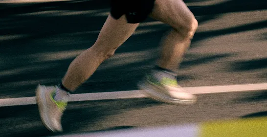 Close-up of a runner's legs in motion on a dark asphalt road with white lane markings.