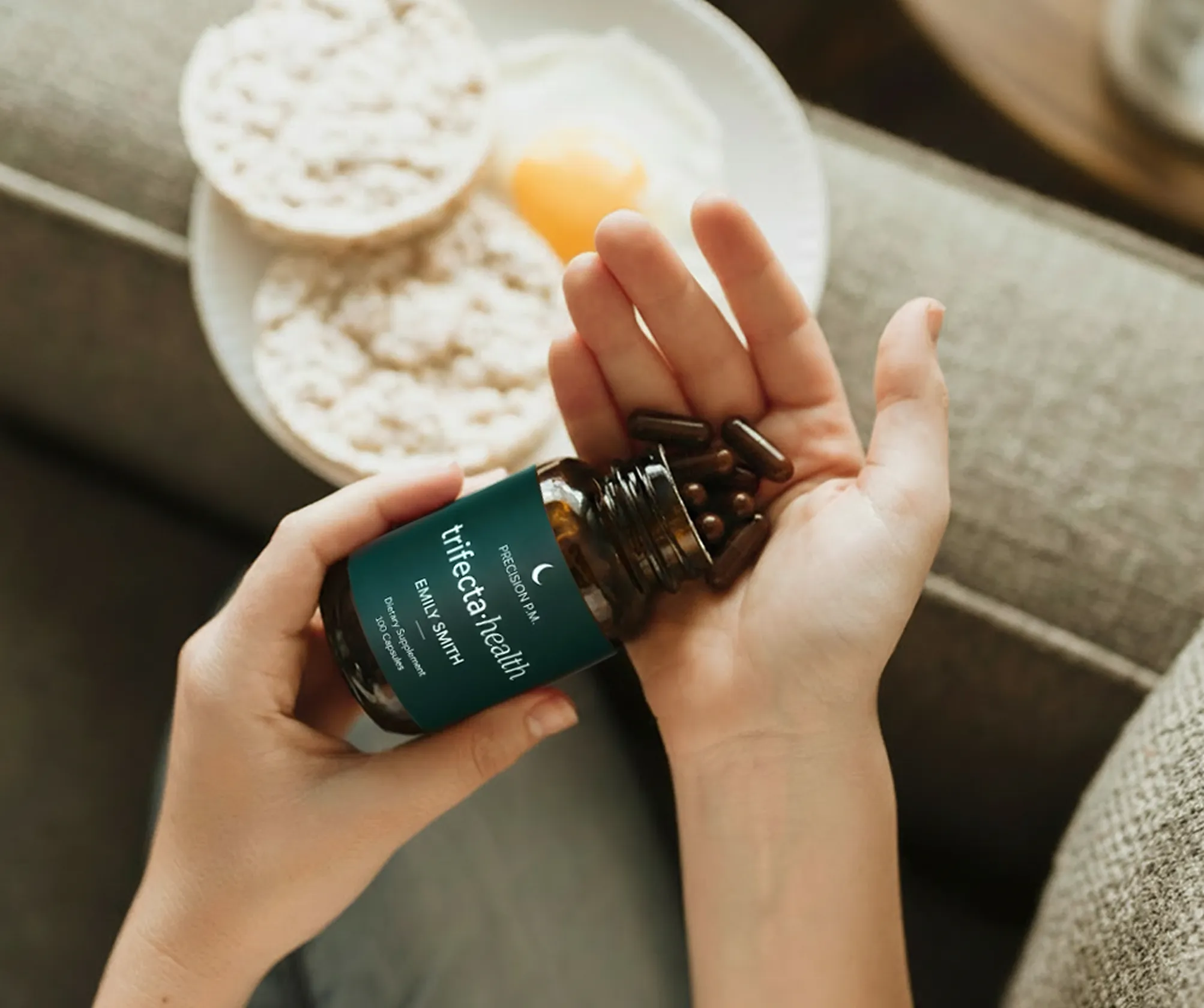 Person pouring dark capsules from a Trifecta Health bottle labeled Emily Smith into their hand.