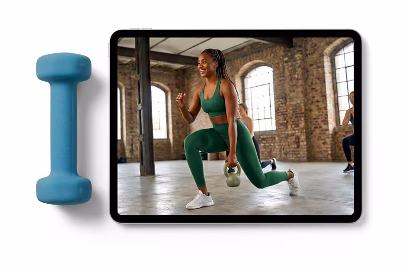 Woman in green workout clothes lunging with a kettlebell in an industrial-style gym on a tablet screen.