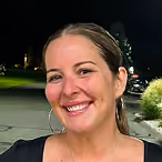 Smiling woman with dark hair wearing hoop earrings in an outdoor nighttime setting.
