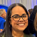 Smiling woman with glasses and long dark hair indoors at an event.