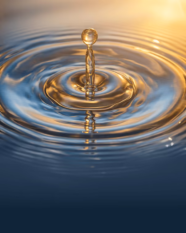 A single water droplet rising from the surface with ripples in blue and gold light.