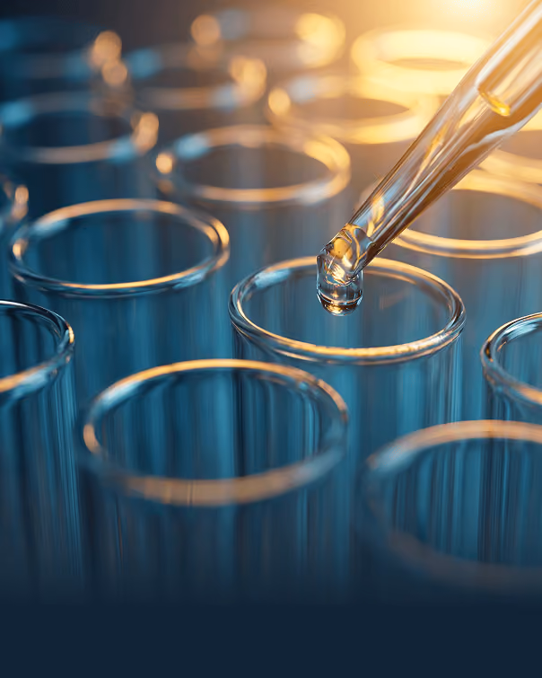 Dropper releasing liquid into one of several empty glass test tubes in blue light.