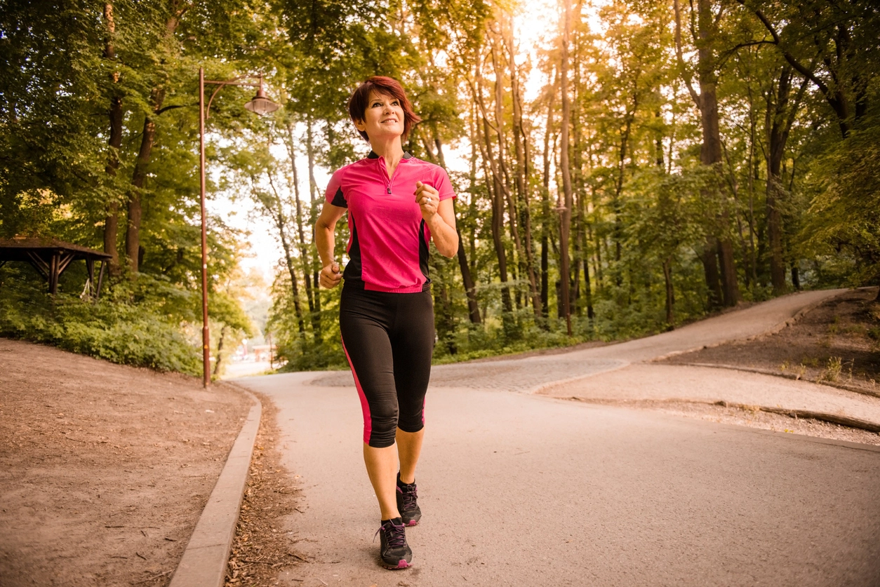 Woman jogging on a wooded path at sunset for an article about IGF-1 testing and growth hormone health.