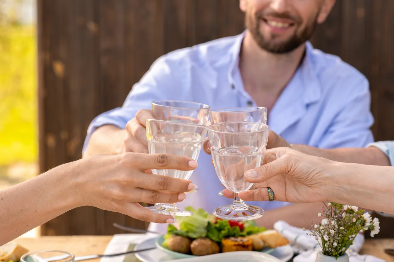 Friends sharing dinner on a sunlit patio with sparkling water for an article about GLP-1s and alcohol.