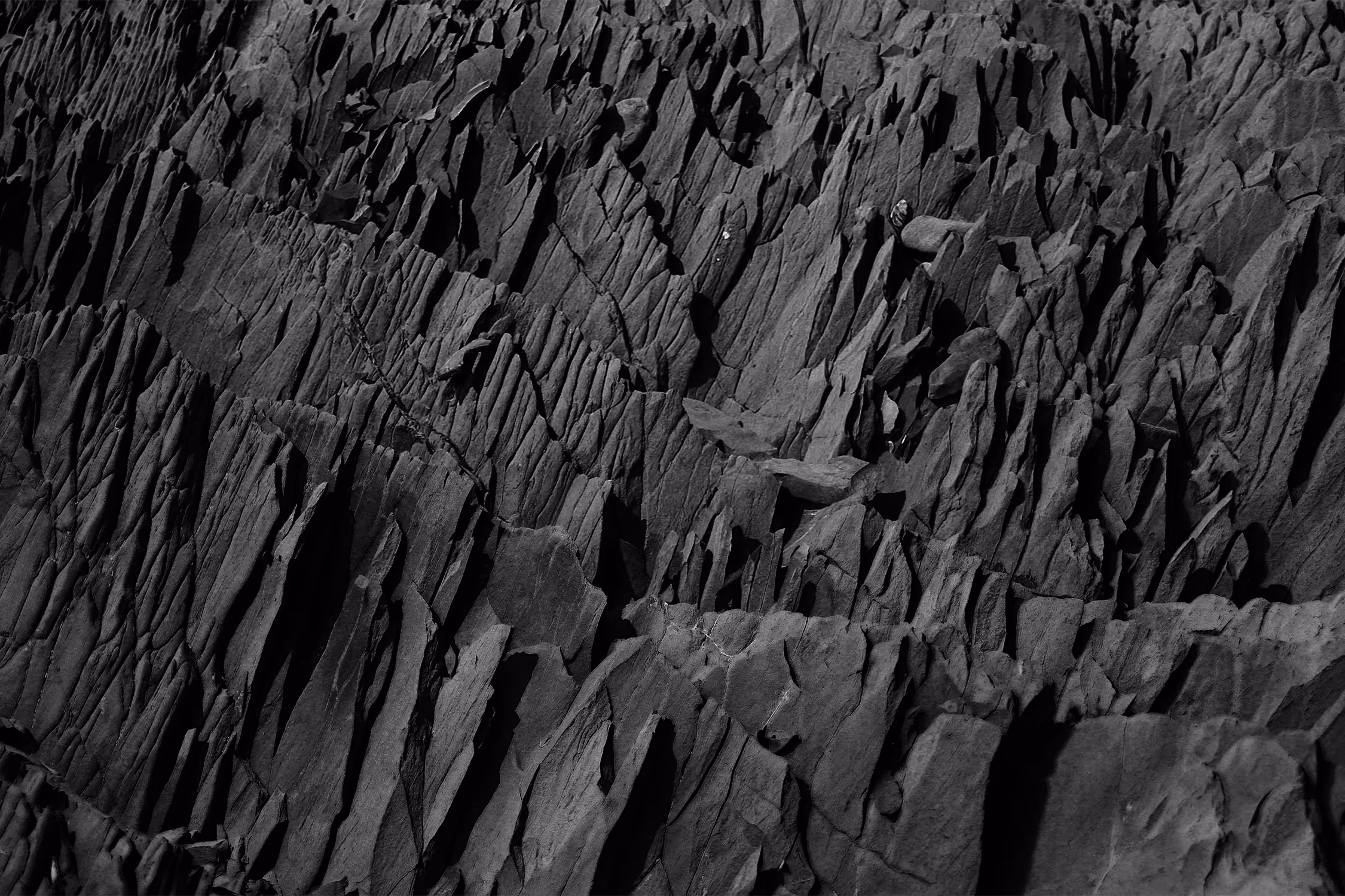 Close-up of dark, jagged layered rock formations with sharp ridges and deep crevices.