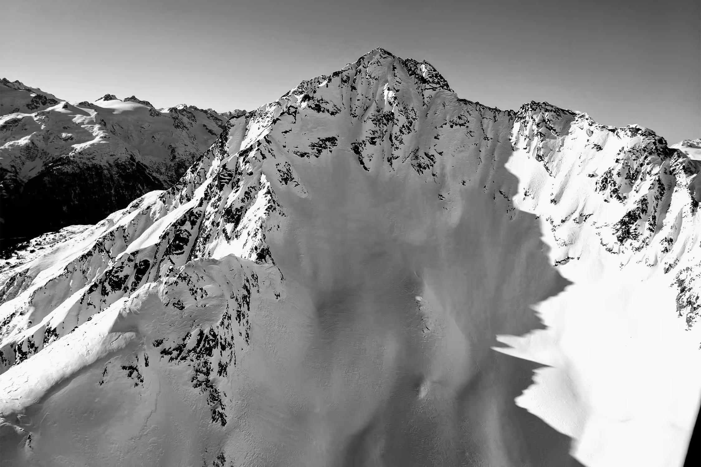 Snow-covered mountain peaks casting shadows under a clear sky in black and white.