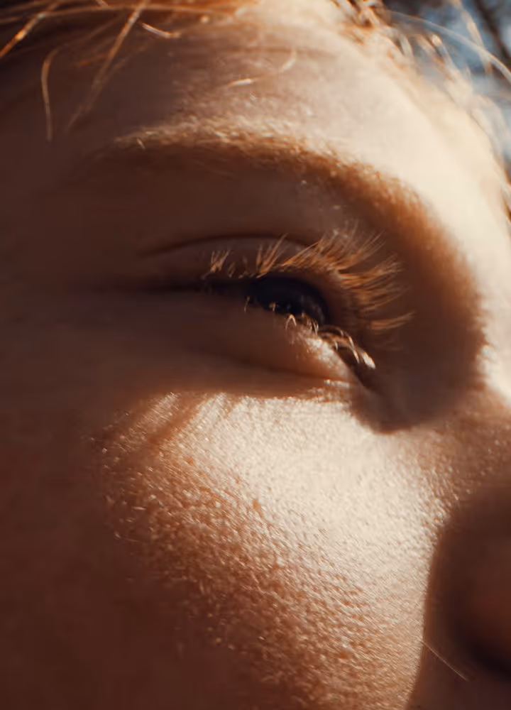 Close-up of a person's eye with long eyelashes and sunlight casting shadows on their skin.
