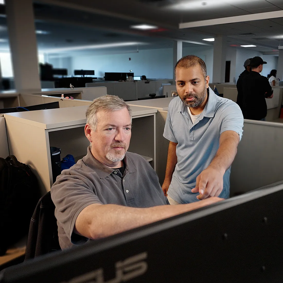 Two coworkers reviewing work on a computer in an open office