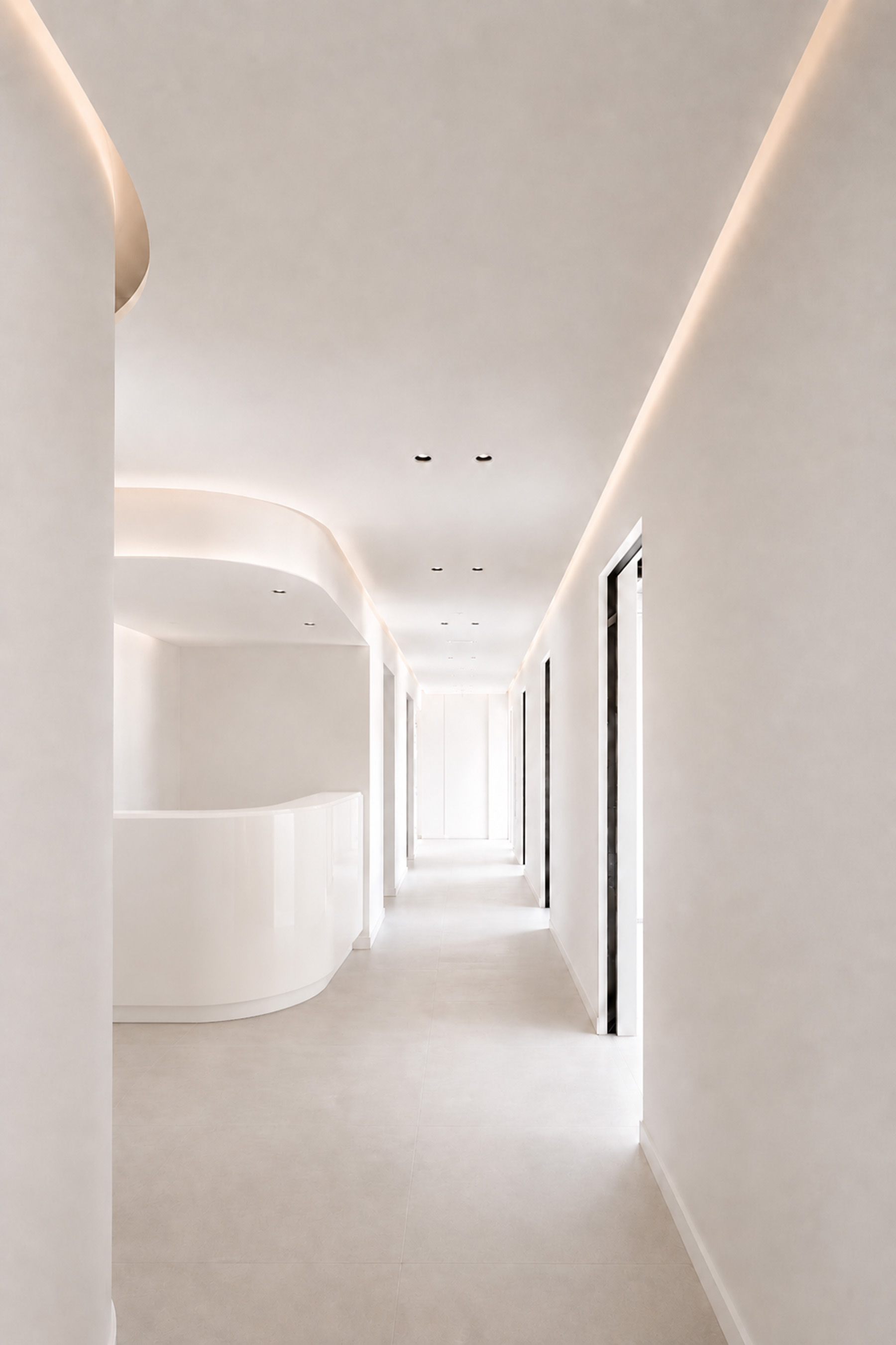 Minimalist white hallway with recessed lighting and curved wall detailing.