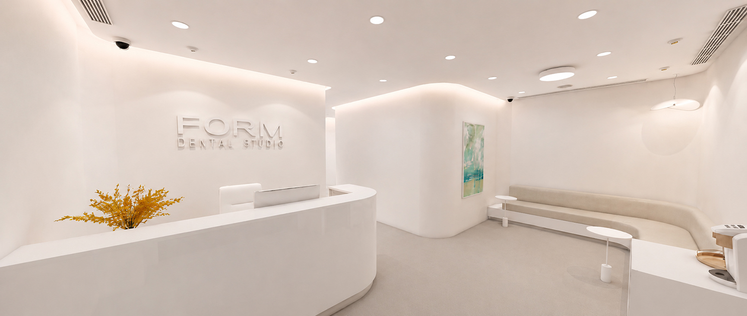 Minimalist white dental studio reception with curved desk, beige seating, and yellow flowers.