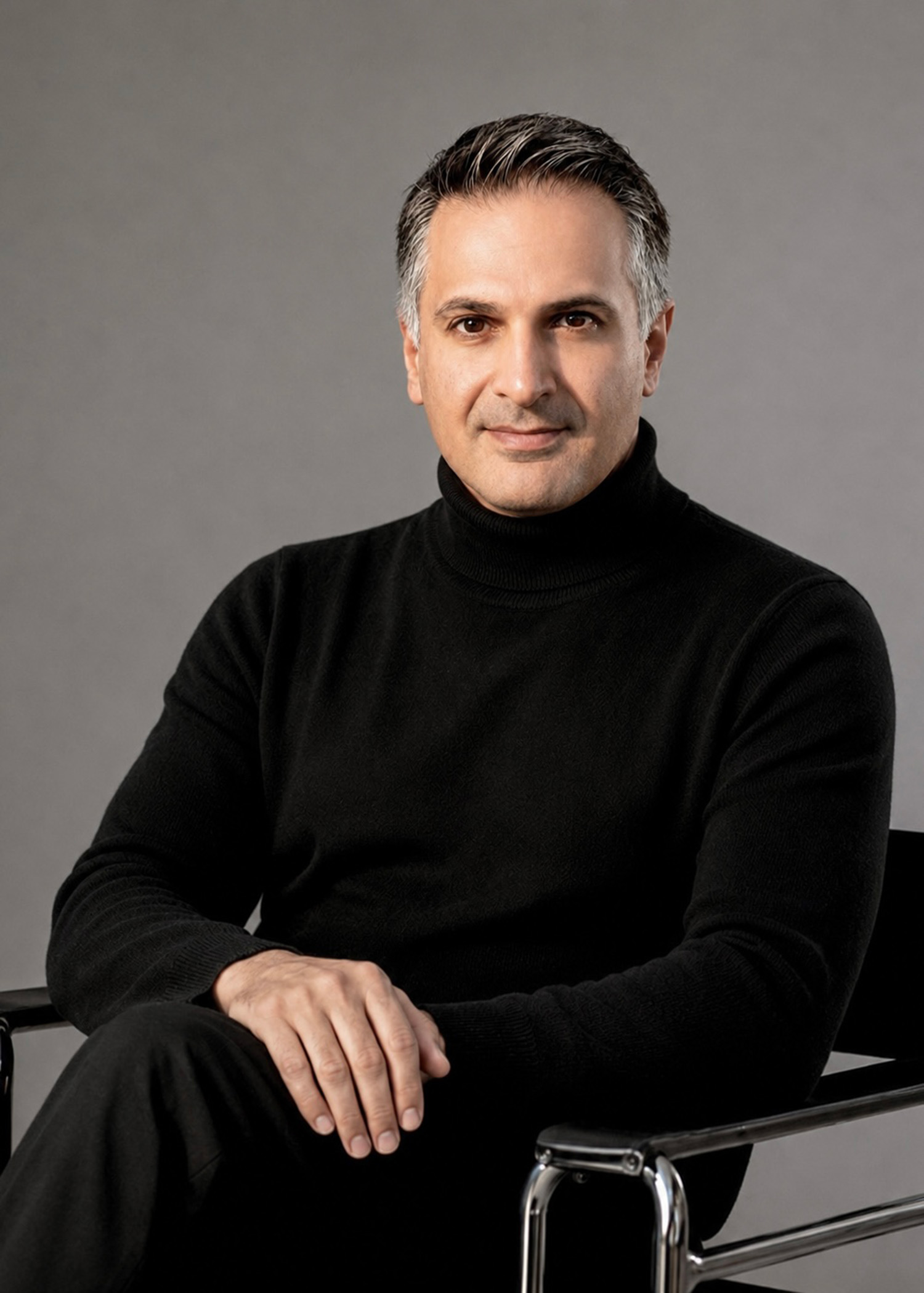 Man with salt-and-pepper hair wearing a black turtleneck sitting in a modern chair.