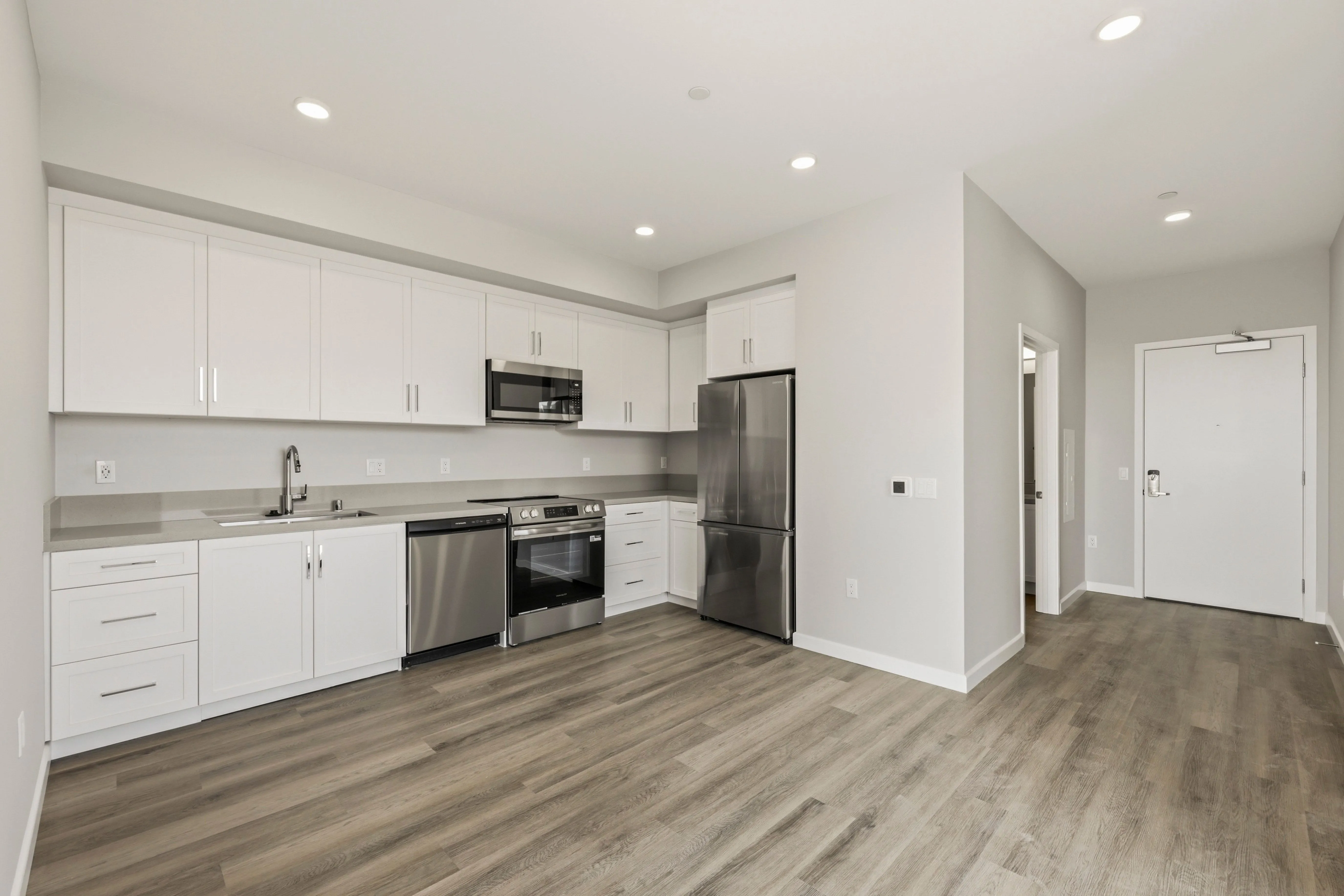 Modern kitchen with white cabinets, stainless steel appliances, gray countertops, and wood laminate flooring.