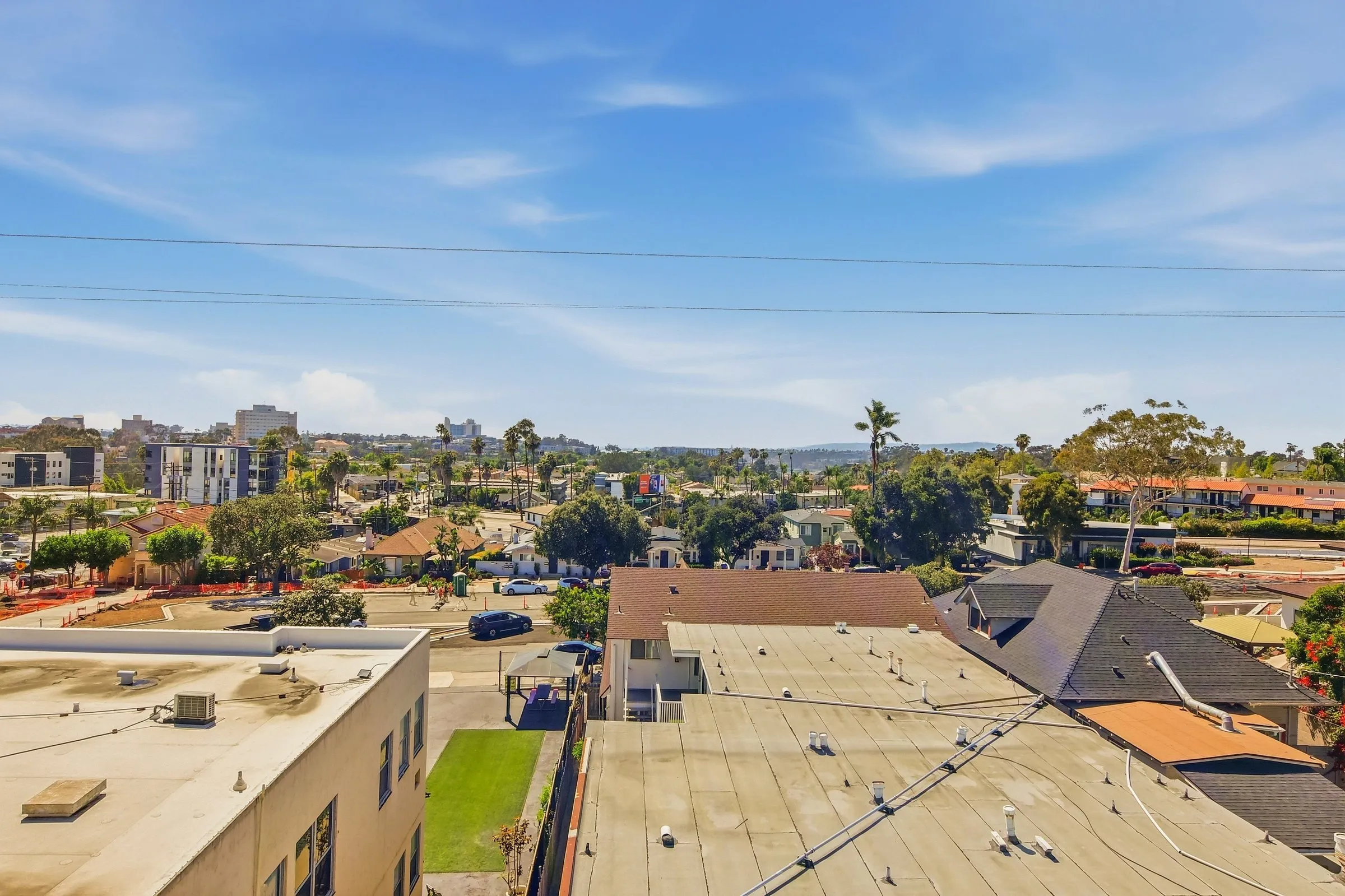 Urban neighborhood with residential buildings, palm trees, and a clear blue sky with light clouds.