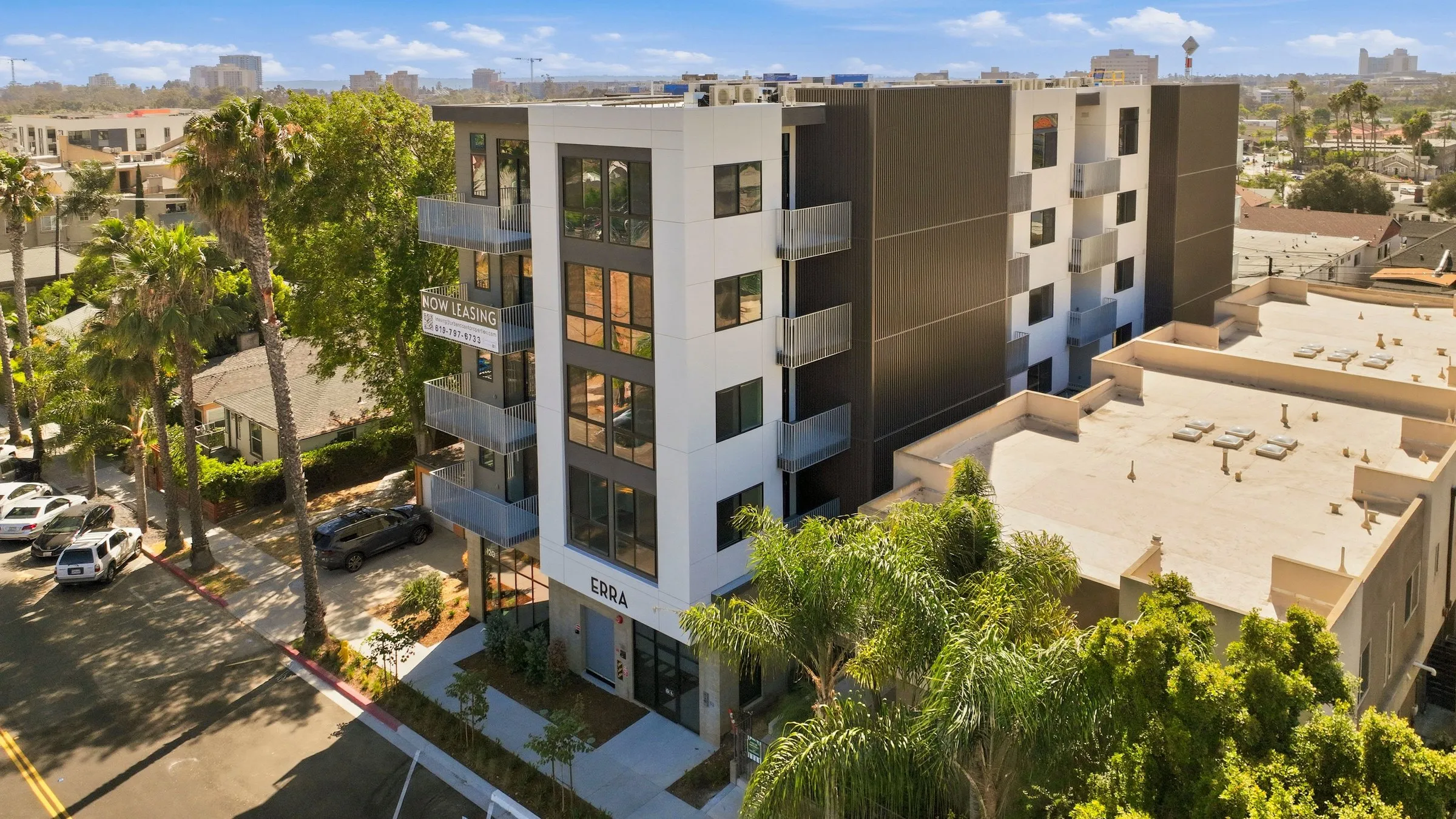 A rooftop patio with people socializing, grilling food, and dining with a city view in the background.