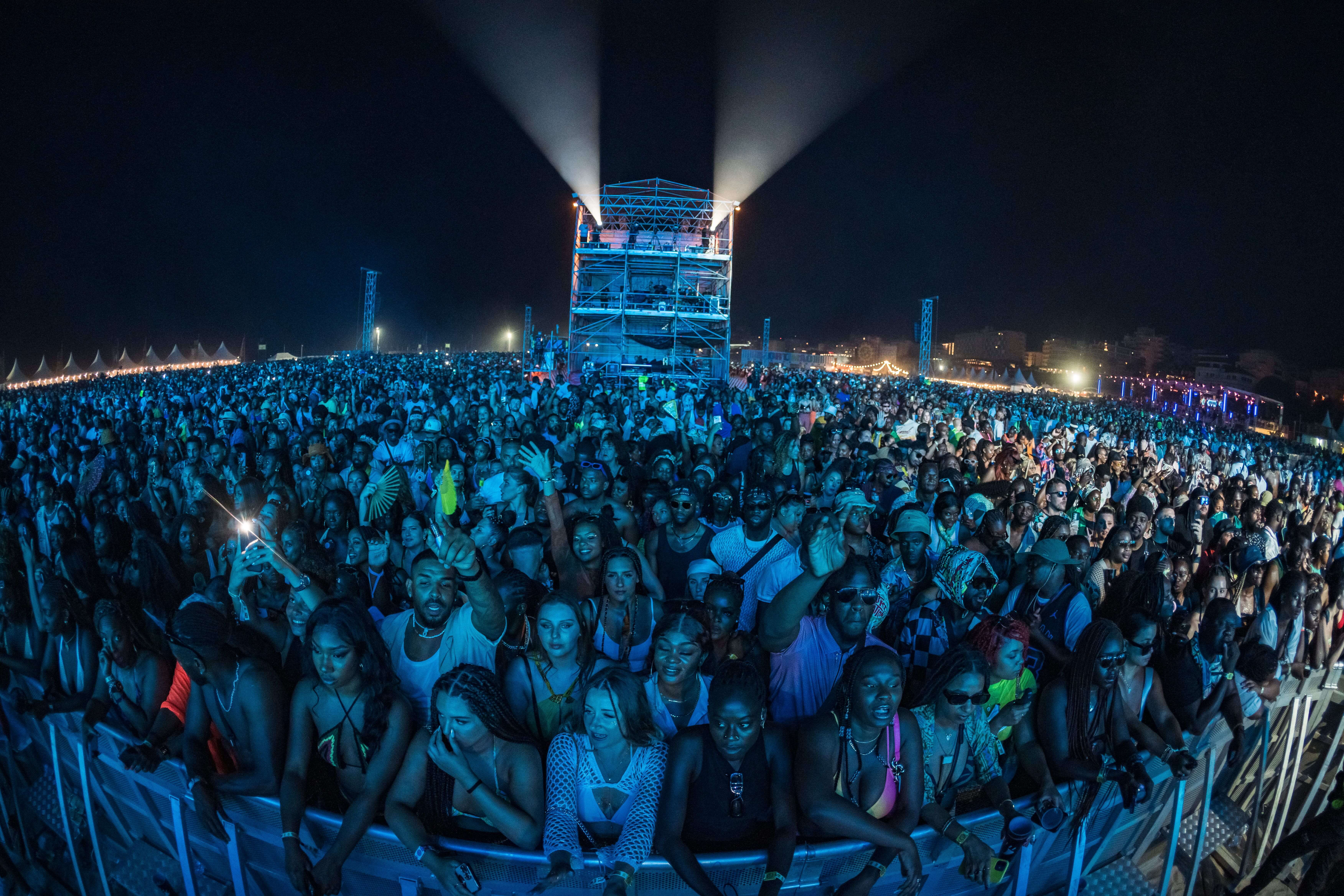 Large nighttime crowd at a music festival with a light tower in the center background.