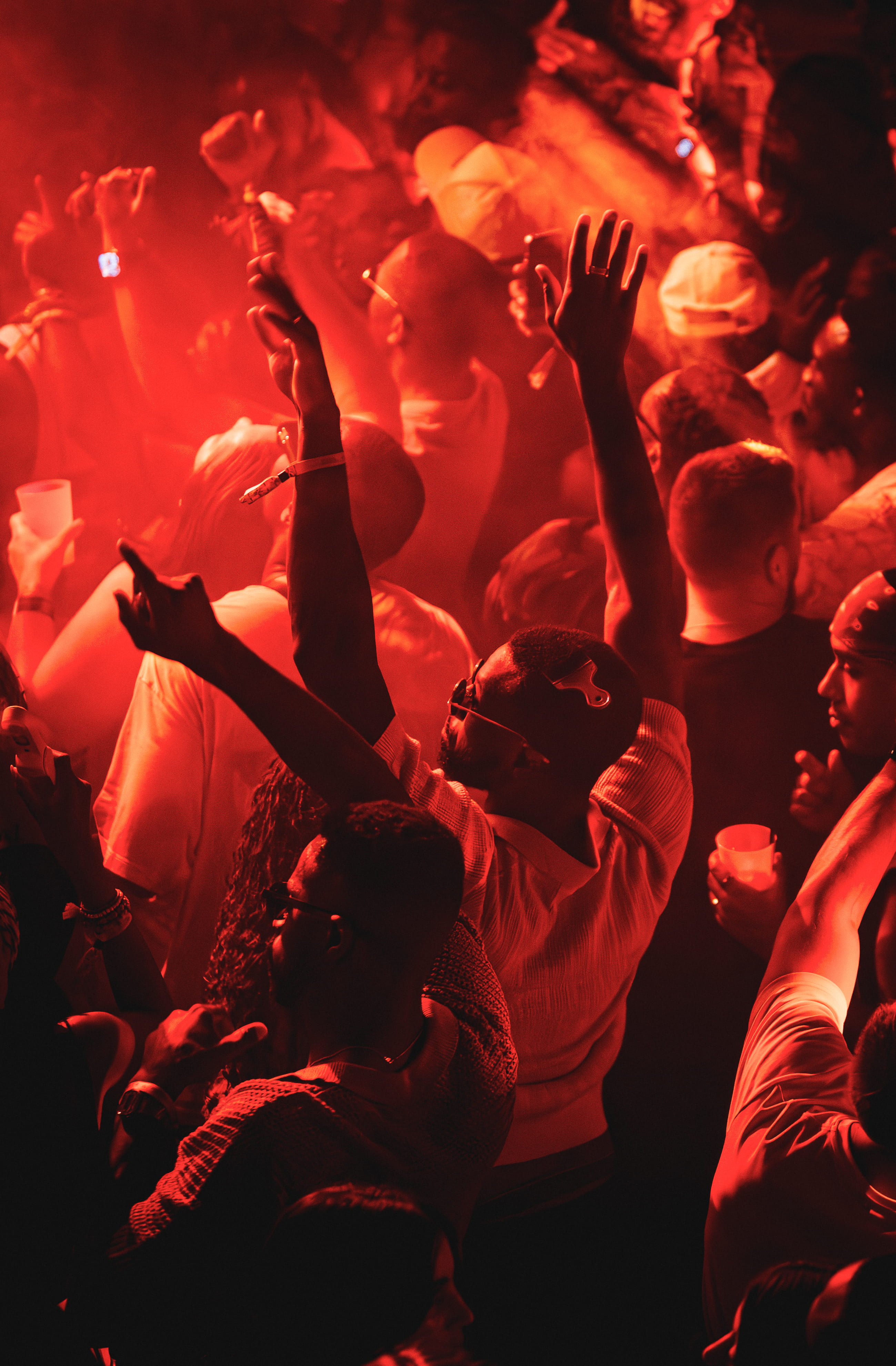 People dancing and raising hands at a crowded party with red lighting.