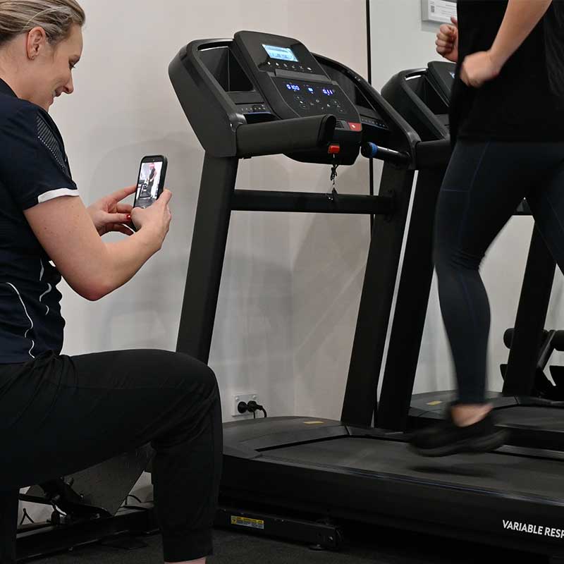 Person running on treadmill while another records the session with a smartphone indoors.