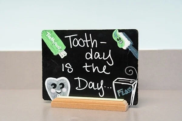 Chalkboard sign reading Tooth-day is the Day beside a toothbrush and floss
