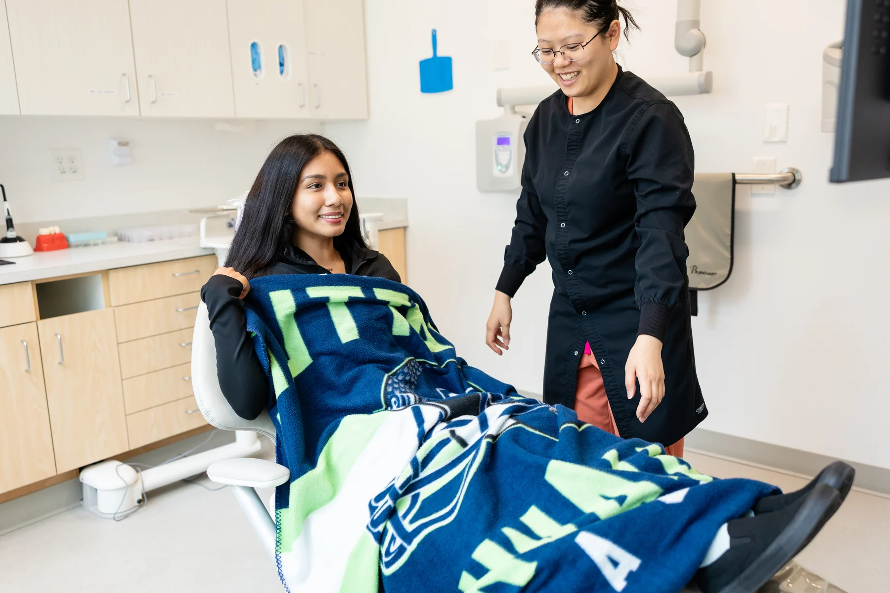 Patient resting under a blanket in the dental chair while a team member checks in