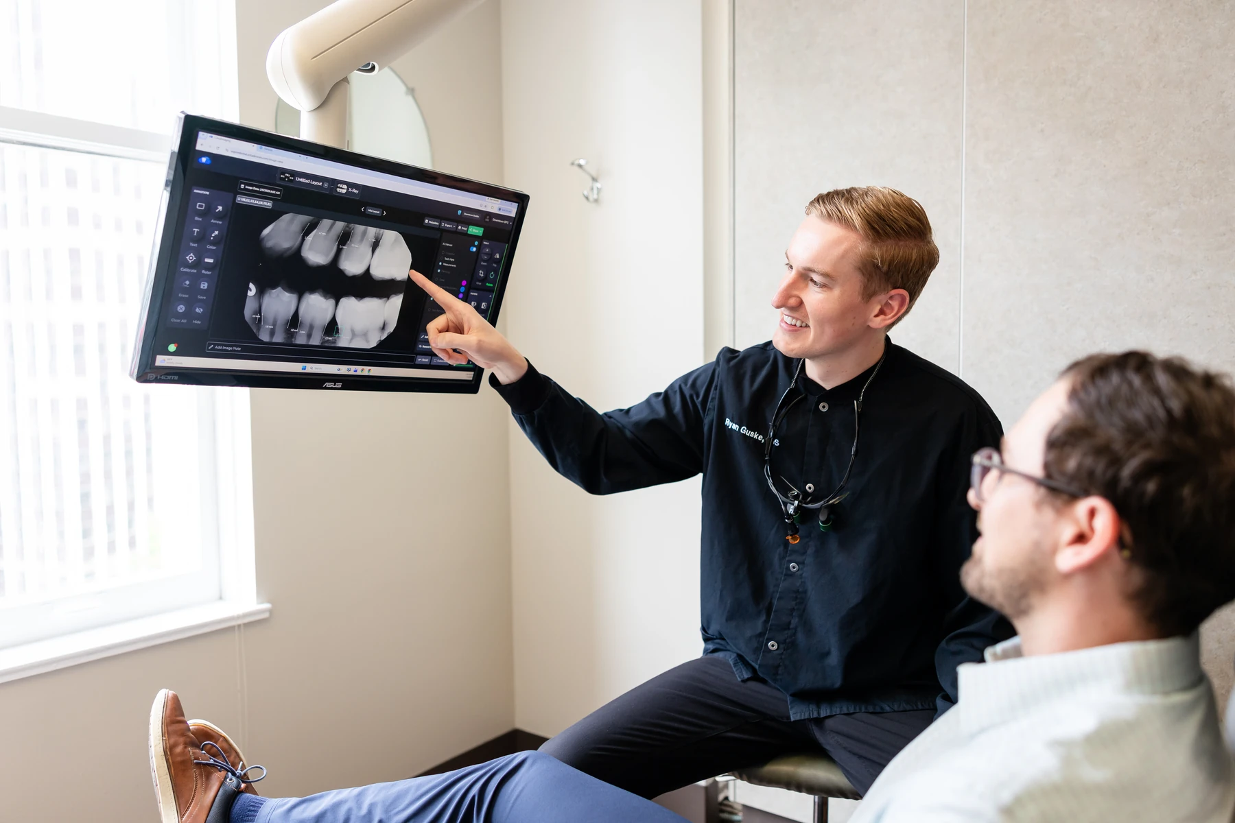 Dentist reviewing X-ray images on screen with a patient