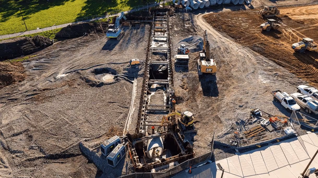 Aerial view of a construction site with heavy machinery and a long trench in the center.