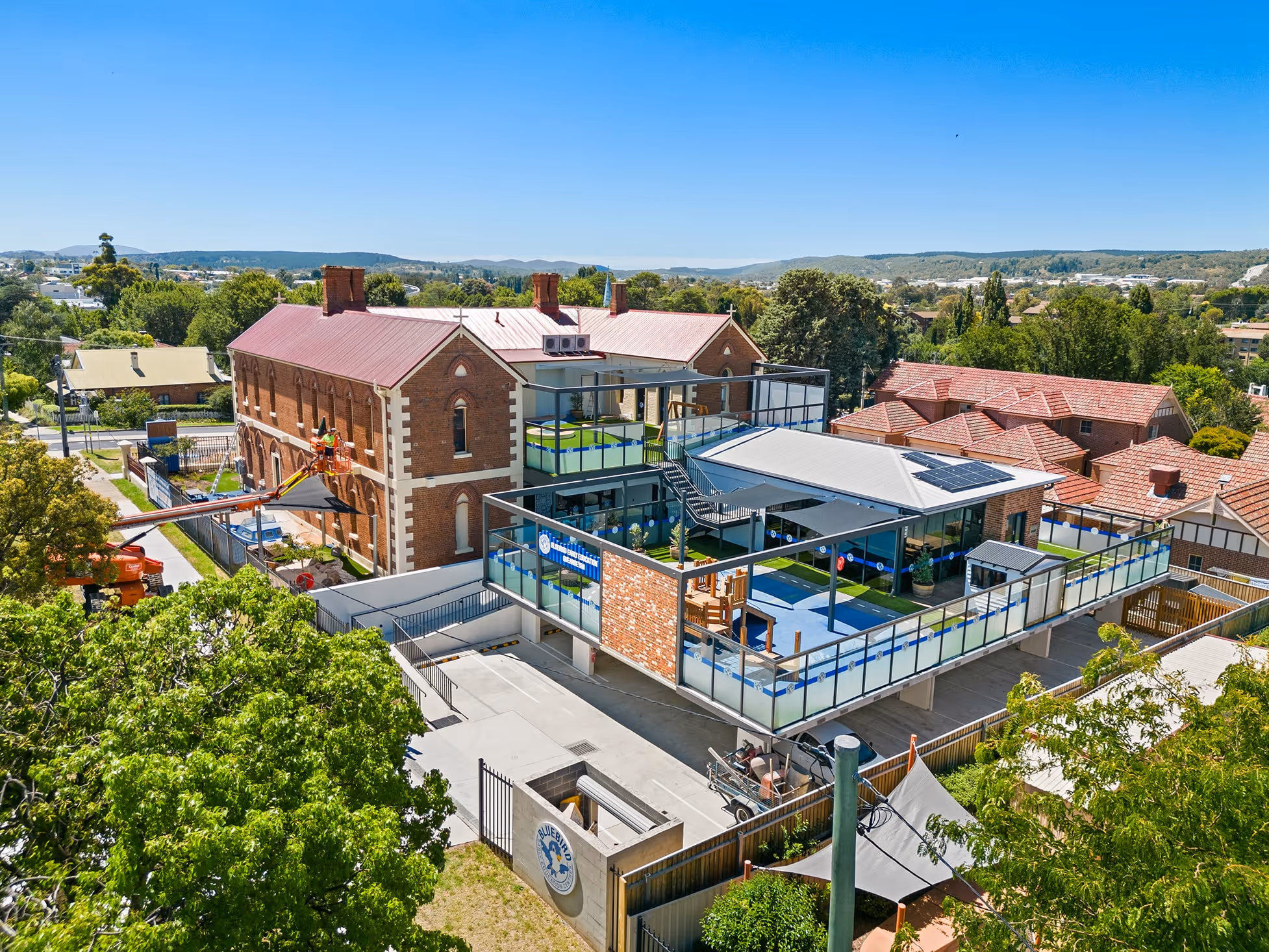Renovated brick building with a modern glass structure and outdoor playground on a sunny day.