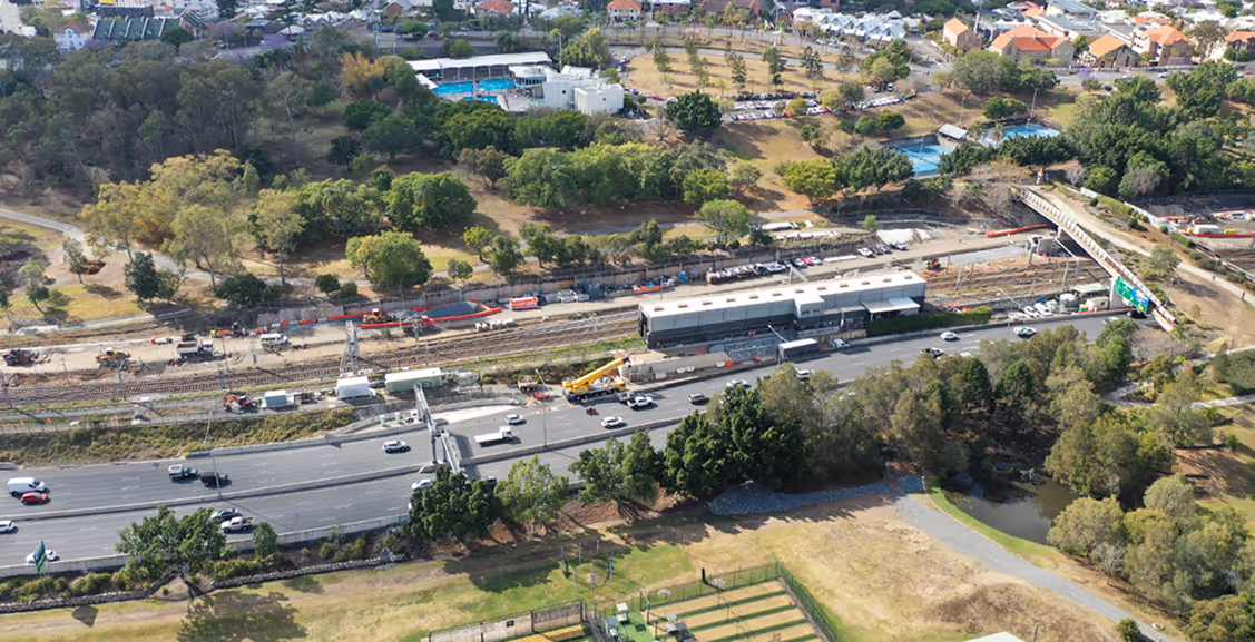 Aerial view of a road and railway construction site surrounded by trees and residential areas.