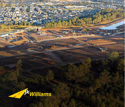 Aerial view of a large construction site near residential homes and a water body in the distance.