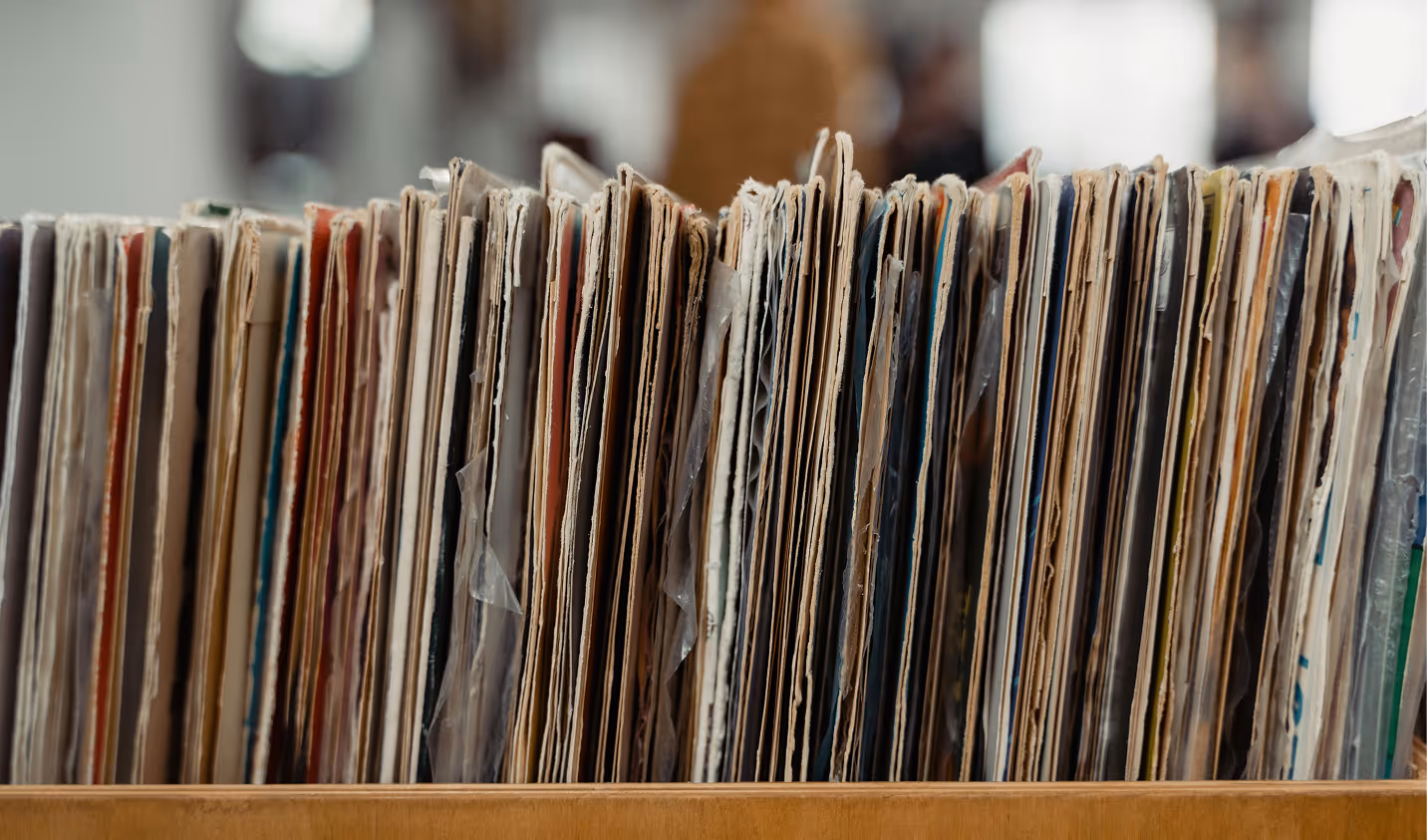 Close-up of a row of vintage vinyl record sleeves stored upright in a wooden crate. (Tima Miroschnichenko, pexels)