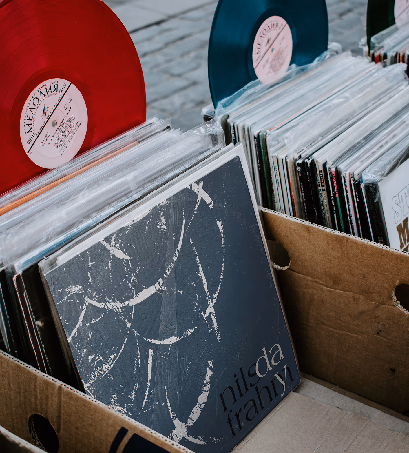 Two vinyl records, one red and one blue, displayed above boxes of records, including one labeled Nilda Frahry. (Matt Smith, behance)