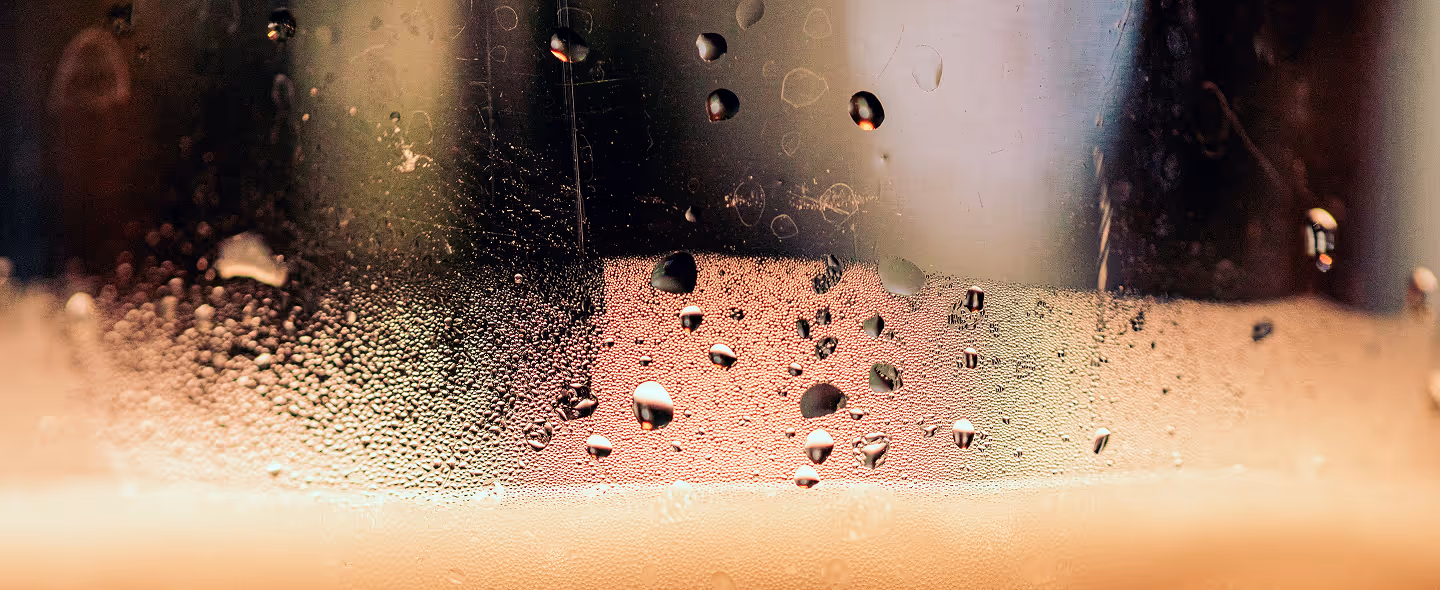 Close-up of condensation droplets on the inside of a glass with a light pink and orange background. (Timothy Dykes, unsplash)